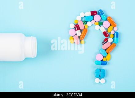 Un point d'interrogation de la mise en place de pilules de médicaments avec le médicament en bouteille sur fond bleu. Banque D'Images