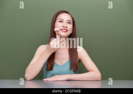 Photo portrait d'une jeune femme qui a l'air d'une utilisation détendue tout en utilisant un rouleau à cadran en quartz rose naturel. Banque D'Images