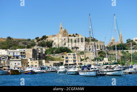 Vue sur le port de plaisance et l'église de la Madonna de Lourdes à Triq Lourdes, Għajnsielem, Malte. Banque D'Images