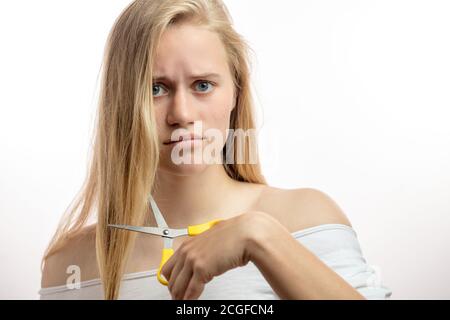 Frustrée jeune femme étant bouleversée et désespéré avec la mauvaise condition de ses cheveux longs blonds décide de couper les extrémités. Soins capillaires, Beauté et Santé Banque D'Images