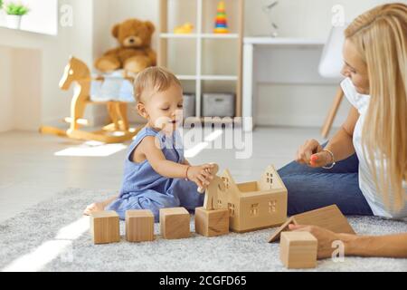 Joyeux baby-sitter et petit enfant jouant avec des blocs de bois dans une chambre confortable Banque D'Images