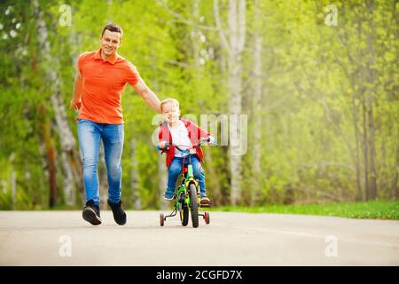 Papa apprend à son petit fils à faire du vélo dans le parc, à garder l'équilibre, à s'amuser en famille. Concept de fête des pères Banque D'Images