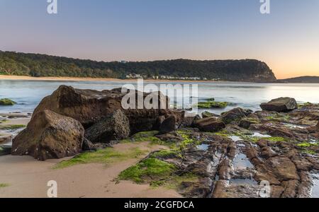 Mer calme et rochers vert mousse se lever à Pearl Beach sur la Central Coast, Nouvelle-Galles du Sud, Australie. Banque D'Images