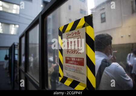 Tokyo, Japon. 10 septembre 2020. Un homme fume une cigarette à côté d'un signe de distanciation sociale du virus Corona à l'intérieur d'une zone fumeurs désignée près de la gare de Toranomon dans le centre de Tokyo. Crédit : SOPA Images Limited/Alamy Live News Banque D'Images