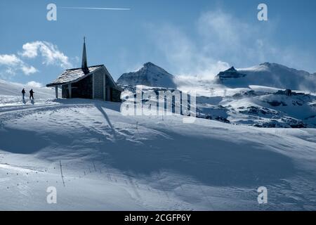 Zermatt, Suisse - février 19 2020 : la chapelle de Riffelberg dans un paysage de neige interminable d'hiver avec deux randonneurs. Banque D'Images