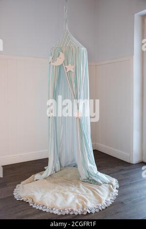 Marquise bleue avec oreillers et jouets suspendus en bois. Chambre confortable pour enfants avec baldaquin avec lune et étoiles. Tente pour enfants. Intérieur élégant de la chambre de bébé scandinave Banque D'Images