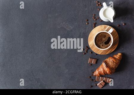 Tasse de café, lait et croissant sur fond noir, vue de dessus avec espace pour les copies. Banque D'Images