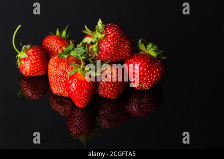 Quelques fraises mûres reposent sur un fond de verre noir et sont reflétées dans celui-ci. Touche Bas Banque D'Images