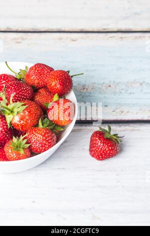 Les baies de fraises mûres se trouvent dans une assiette haute blanche, qui repose sur un fond en bois clair. Emplacement pour l'espace de copie Banque D'Images