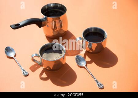 Un matin ensoleillé, deux tasses de café et une casserole de café se tiennent sur fond orange. Petit déjeuner.orientation horizontale Banque D'Images