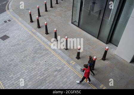 Comme les travailleurs de Londres continuent de travailler en grande partie de chez eux pendant la pandémie du coronavirus, deux personnages se promoncent dans un paysage urbain de rues avec des marquages routiers et des bornes de circulation dans la City de Londres, le quartier financier de la capitale, le 4 septembre 2020, à Londres, en Angleterre. Banque D'Images