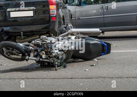 une moto cassée près de la voiture. un accident sur la route dans la ville par une journée ensoleillée impliquant une moto et une voiture. Banque D'Images