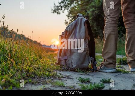 Les pieds de l'homme sont sur la piste dans le champ contre le ciel avec un coucher de soleil en été, environ les pieds de l'homme est un sac à dos. Le concept de voyage Banque D'Images