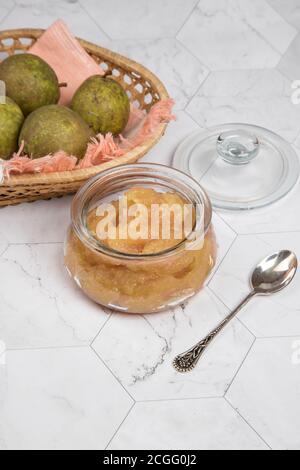 Pot en verre avec des poires écrasées et des poires fraîches dans une assiette en osier sur fond clair . Orientation verticale. Banque D'Images