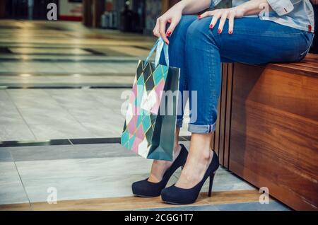 Fille dans les talons hauts et sacs d'achats - une fille en jeans se trouve sur un banc et chatter après l'achat cadeaux Banque D'Images