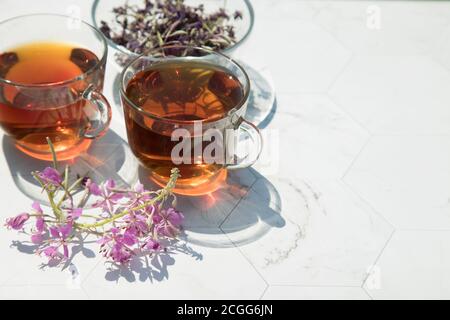 Chamaenerion angustifolium thé (cyprès, saule rose, Ivan-thé) avec fleurs sèches et fraîches pour la décoration dans deux tasses en verre sur un fond clair, dri Banque D'Images