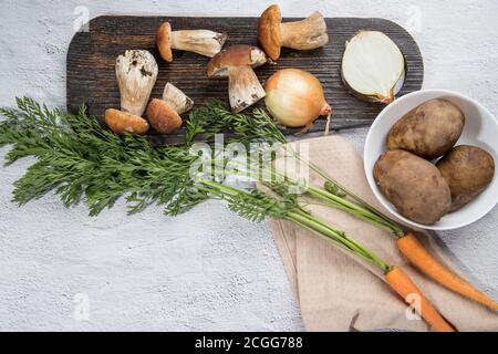 Divers ingrédients pour cuisiner divers plats de champignons porcini de forêt sur un fond léger - champignons, carottes, pommes de terre, oignons, avec un bois Banque D'Images