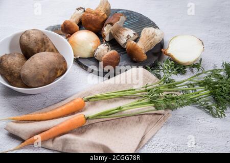 Divers ingrédients pour la cuisson des champignons porcini de forêt sont disposés sur un fond clair - champignons, carottes, pommes de terre, oignons, avec une coupe ronde Banque D'Images