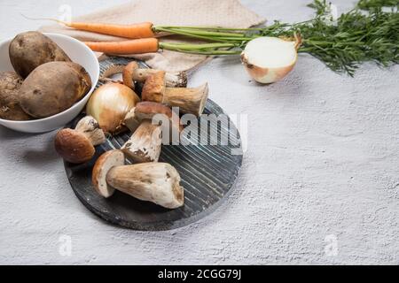 Divers ingrédients pour la cuisson des champignons porcini de forêt sont disposés sur un fond clair - champignons, carottes, pommes de terre, oignons, avec une coupe ronde Banque D'Images