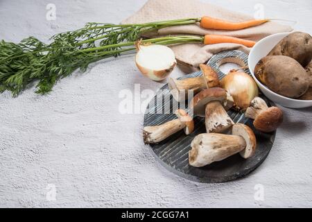 Divers ingrédients pour la cuisson des champignons porcini de forêt sont disposés sur un fond clair - champignons, carottes, pommes de terre, oignons, avec une coupe ronde Banque D'Images