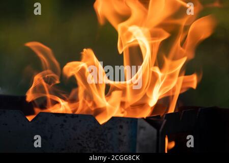 Flammes chaudes orange qui brûlent dans le gril en métal en gros plan. Foyer extérieur chaud avec un arrière-plan flou Banque D'Images