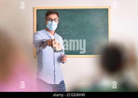 Professeur d'école primaire protégé avec masque en raison du risque de l'infection à coronavirus demande la leçon en classe Banque D'Images