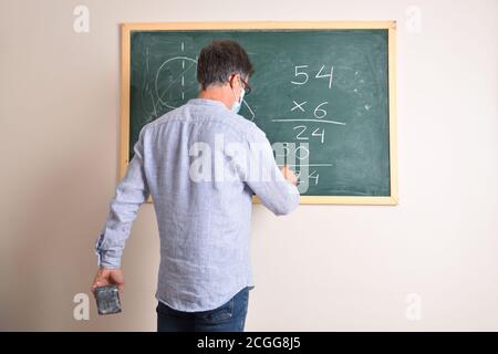 Professeur d'école primaire protégé avec un masque en raison de risque d'infection à coronavirus résolvant la multiplication dans la classe Banque D'Images