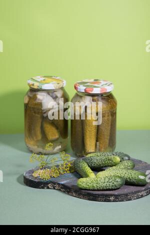 Boîtes de cornichons et de cornichons. Pickles marinés sur une planche à découper en bois avec des herbes. Orientation verticale Banque D'Images