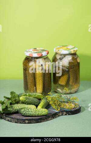 Deux boîtes de cornichons et de cornichons. Pickles marinés sur une planche à découper en bois avec des herbes. Orientation verticale Banque D'Images