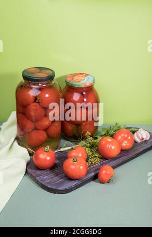 Tomates mûres marinées en pots . Des tomates fraîches avec de l'ail et des herbes sont sur la planche à découper. Orientation verticale. Banque D'Images