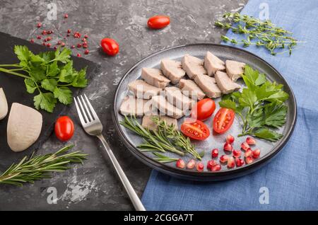 Langue de porc bouillie avec tomates et herbes sur fond de béton noir et tissu de lin bleu. Vue latérale, gros plan. Banque D'Images