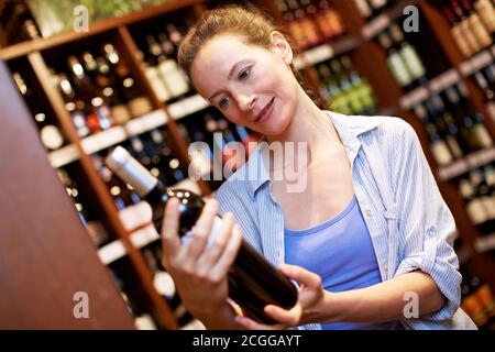 Une femme âgée achète une bouteille de vin rouge dans le supermarché Banque D'Images