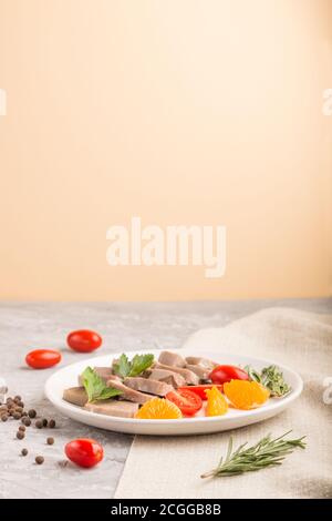 Langue de porc bouillie avec tomates et herbes sur fond gris et orange et toile de lin. Vue latérale, espace de copie. Banque D'Images