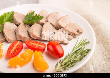 La langue de porc bouillie avec des tomates et des herbes sur fond de béton gris et le tissu de lin. Vue latérale, gros plan, mise au point sélective. Banque D'Images