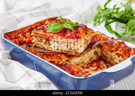 Cassolette de lasagne italienne avec tofu ferme, champignons, sauce tomate cuite au four, servie sur un plat de cuisson au basilic frais sur un fond de bois blanc Banque D'Images