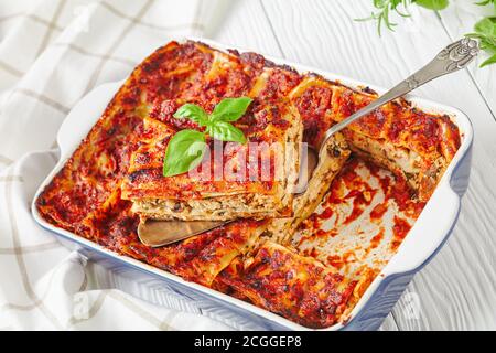 Plat de cuisson avec lasagnes végétariennes de tofu ferme, champignons, sauce passata avec feuilles de basilic frais sur fond de bois blanc, gros plan Banque D'Images
