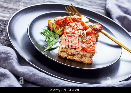 Une portion de lasagne végétarienne au champagnon et sauce tomate bolognaise végétalienne, tofu et assaisonnement italien, servie sur une assiette noire avec du ro frais Banque D'Images