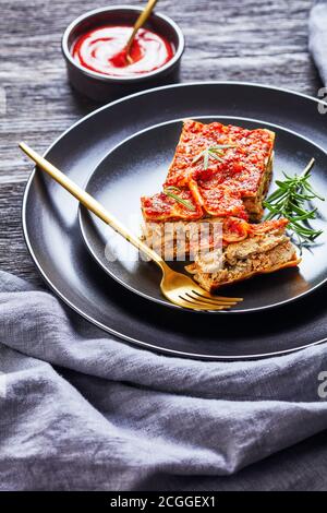 Lasagnes végétaliennes aux épinards tofu avec champagnon et tomate végétarienne bolognaise servie sur une assiette noire à la fourchette et fraîche romarin sur un rus foncé Banque D'Images