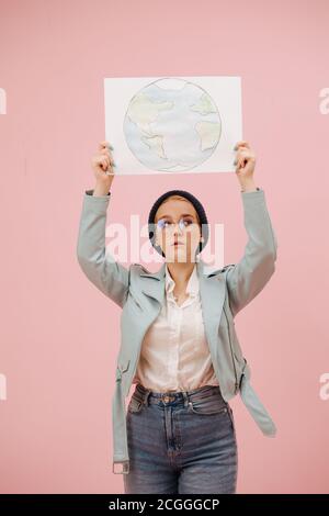 Intéressée écoactiviste femelle dans un chapeau et des verres ronds affiche la bannière de terre Banque D'Images