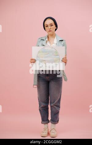 Une écoactiviste féminine sombre et évisse dans une casquette montrant une bannière de terre Banque D'Images