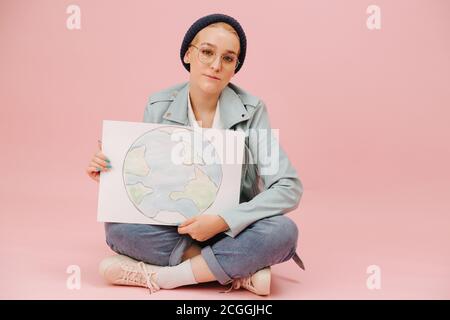 Mignonne écoactiviste dans une casquette avec des pattes croisées bannière de terre Banque D'Images