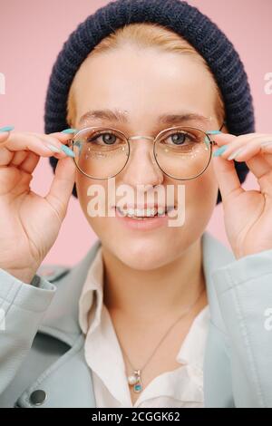 Jeune femme excentrique enthousiaste dans une casquette et des verres ronds. Sur rose. Banque D'Images