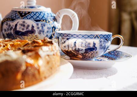 Tarte aux pommes sur un plat blanc, une théière et deux tasses de thé chaud sur une table recouverte d'une nappe blanche. Banque D'Images