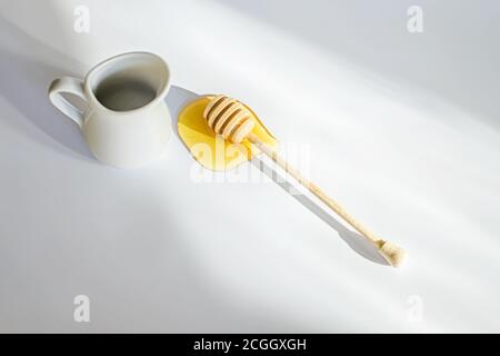 bâton de bois pour le miel dans la flaque de miel de printemps liquide jaune. miels enlever sur fond blanc avec tache de lumière. Banque D'Images