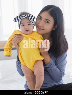 Une maman asiatique joue avec son bébé au lit avec amour et soin. Banque D'Images