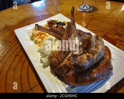 Assiette de viande d'agneau - Chop d'agneau, saucisses de style sud-africain, saucisse de porc sur une assiette avec pommes de terre à l'ail, épinards crémeux et sauce. Banque D'Images