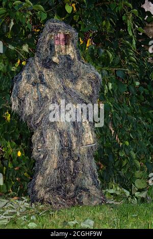 Une personne en camouflage se tient presque invisible devant une haie. Banque D'Images