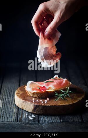 Mettre la main sur des femmes de prosciutto pain sur fond en bois sombre. Cuisine sandwich. Banque D'Images