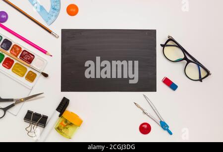 Fournitures de bureau sous forme de cadre, espace pour texte sur un conseil scolaire noir, fond blanc, vue de dessus. Banque D'Images