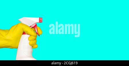Une main dans un gant en caoutchouc tient un pistolet de pulvérisation avec un agent de nettoyage ou de désinfection. Isolé, fond turquoise, espace libre pour le texte. Banque D'Images